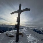 Gipfelkreuz vor verschneiten Bergen.