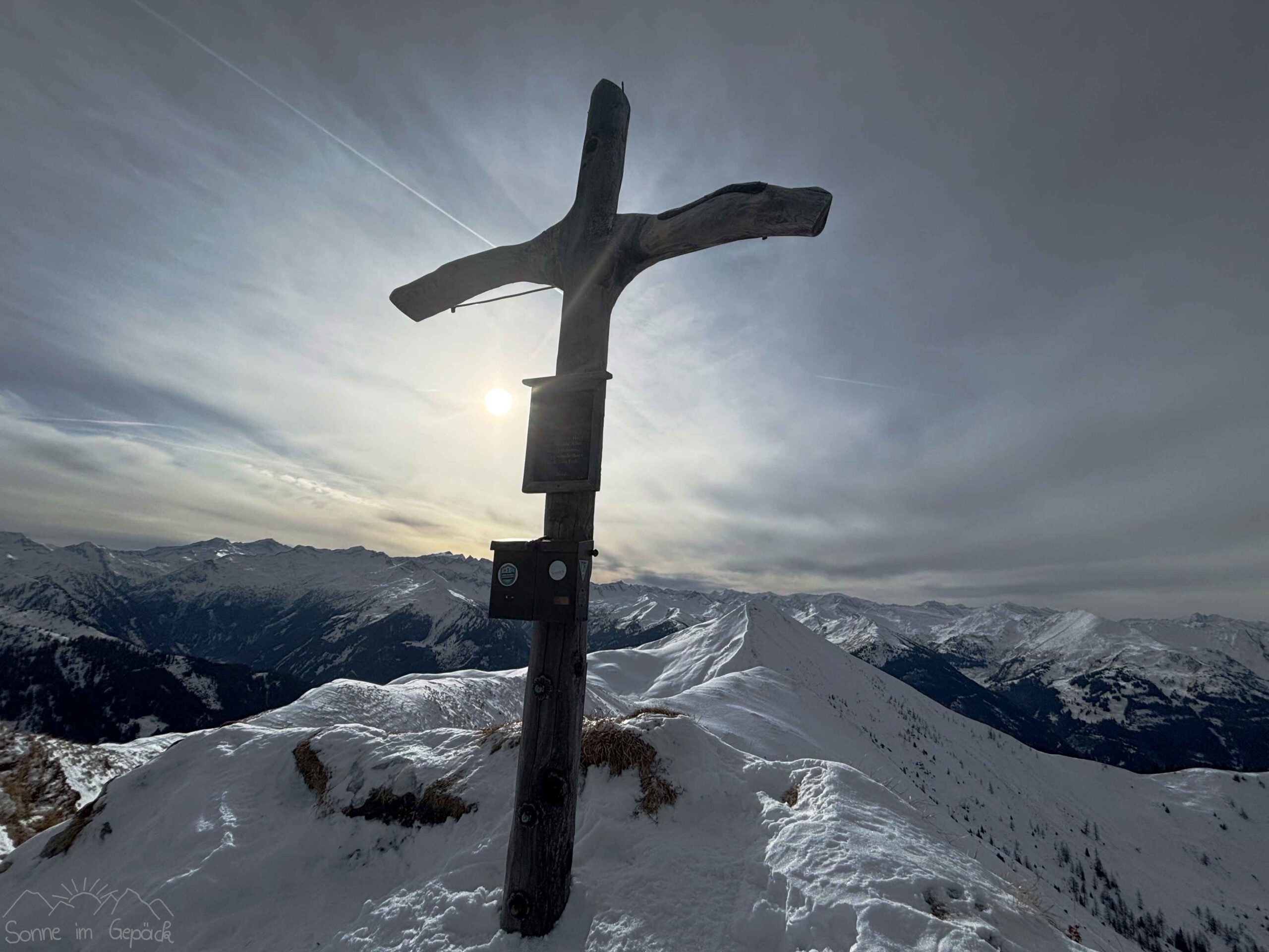 Gipfelkreuz vor verschneiten Bergen.